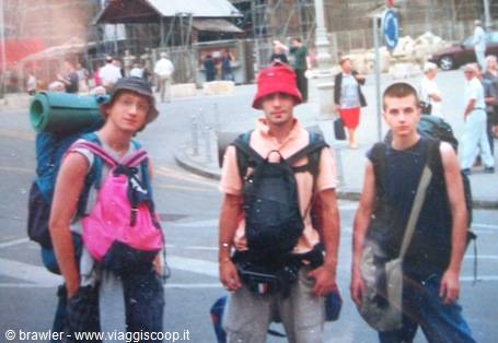Three young backpackers with backpacks and rolled mats crossing an urban square