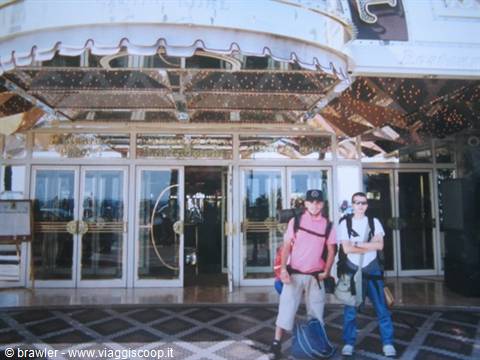 Two backpackers with luggage stand before a mirrored casino entrance