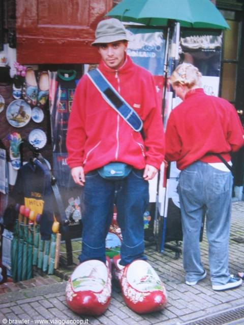 Tourist in red jacket wearing giant painted wooden clogs, Dutch souvenir shop