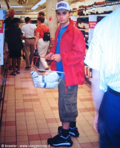Young man in white cap and red jacket holds a basket in a supermarket