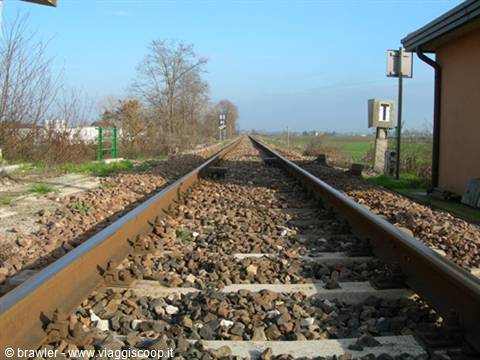 Straight railway tracks on gravel ballast, signal poles and brick building, morning light