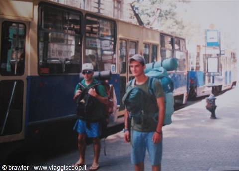 Two backpackers with large packs beside a yellow and blue tram