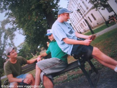 Three smiling guys on a park bench in front of a white building
