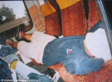 Boy lying asleep on red patterned train seats while traveling