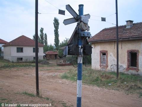 Rusty railway crossing signal on blue pole among abandoned rural houses