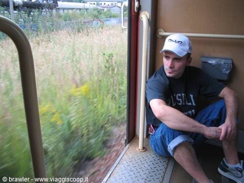 Traveler sitting on the open train door beside green fields