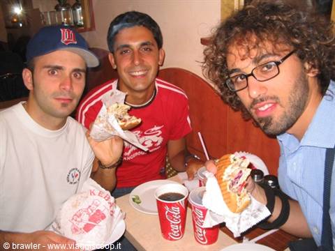 Three smiling friends eating huge sandwiches with Coca-Cola cups in an American diner