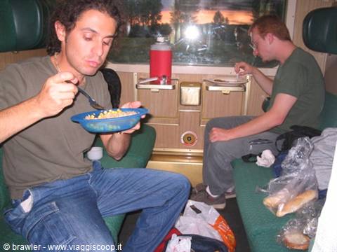 Two travelers eat pasta and bread on green train seats
