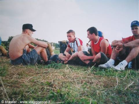 Group of young men in tank tops sitting on grass, chatting and resting