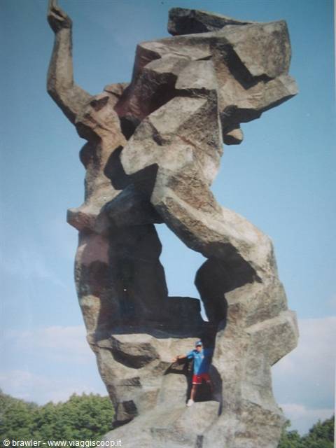 Man standing beneath a monumental angular stone sculpture against blue sky