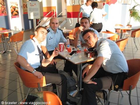 Four men in light blue uniforms sitting at a cafeteria table with soft drinks