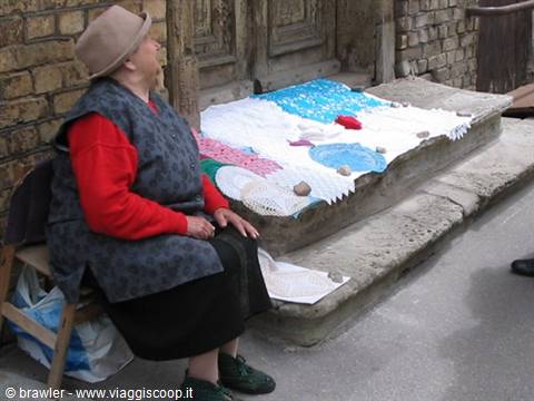 Woman in hat selling handmade crochet lace on old stone steps