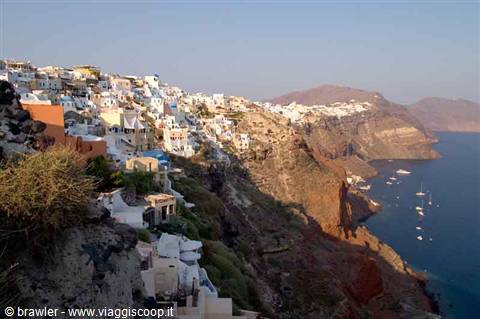 Whitewashed houses carved into Santorini caldera cliff above boats on blue sea