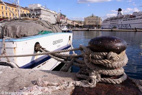 Mooring bollard with ropes in Trieste, boat Orsorosa tied, Jadrolinija ferry behind