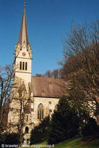 Stone church with tall Gothic spire among bare trees, daylight