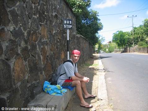 Traveler sitting by a volcanic stone wall, waiting at the bus stop