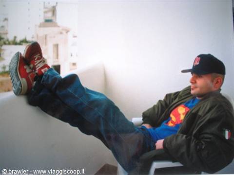 Man in cap and red sneakers relaxing on white chair at a balcony