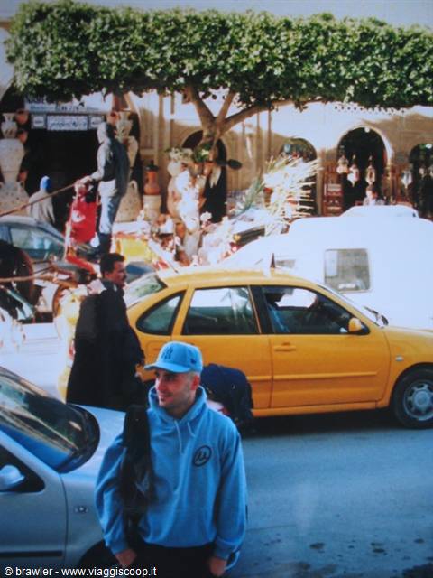 Tourist in blue hoodie and cap beside a yellow taxi on a busy street