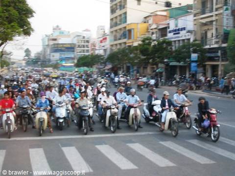 Crowd of scooters waits at the light among Saigon buildings
