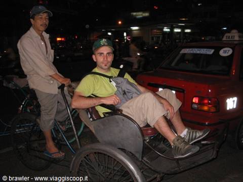 Tourist riding a cycle rickshaw at night beside a red taxi