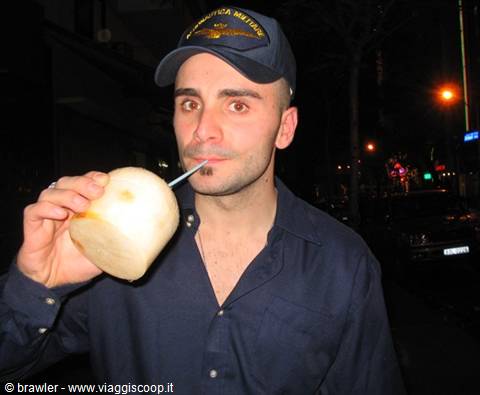 Man in blue cap drinking coconut with straw on a night street