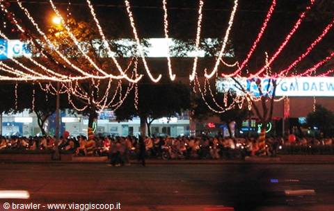 Fairy lights strung above a busy street full of motorbikes, glowing signs