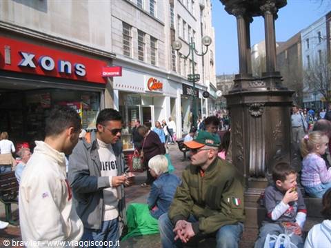 Pedestrians and kids sitting beside an ornate cast-iron column in a pedestrian street