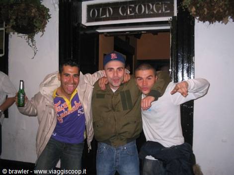 Three friends arm in arm outside the Old George pub, one raising a beer bottle