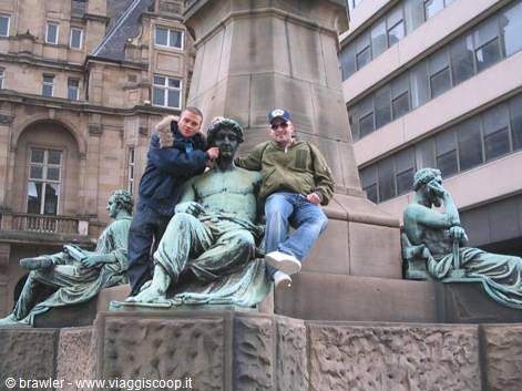 Two tourists sit on the green bronze figures at a monument base
