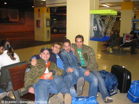 Four young men sitting on wooden benches in a bus station, bags at their feet