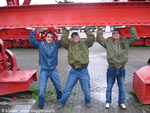 Three friends lifting a red steel beam among old industrial machinery