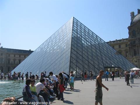 Glass pyramid of the Louvre in Paris, tourists sitting by the fountain