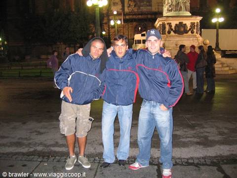 Three friends in blue windbreakers arm in arm near the monument on Milan's Duomo square