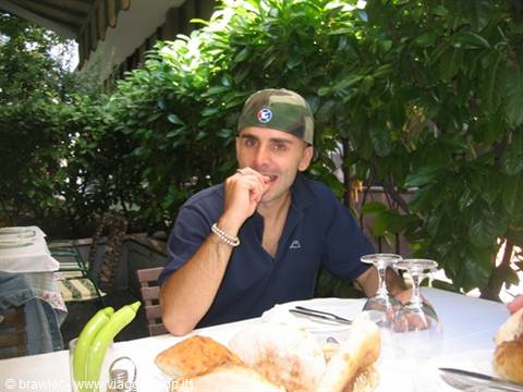 Man in military cap eating bread at an outdoor restaurant table