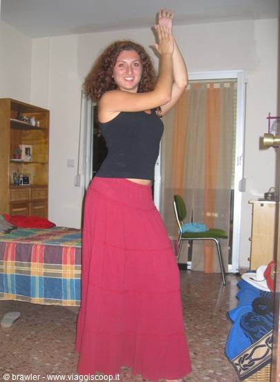 Curly-haired girl dances in a bedroom with bed and orange curtain