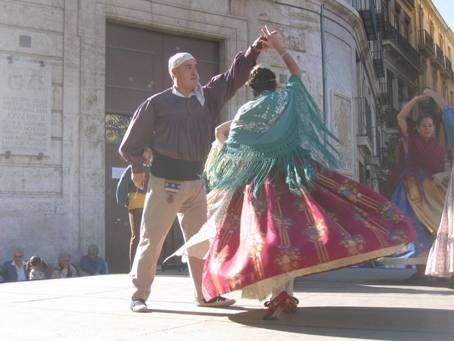 Couple dancing a traditional folk dance in a square, woman in green shawl and red skirt