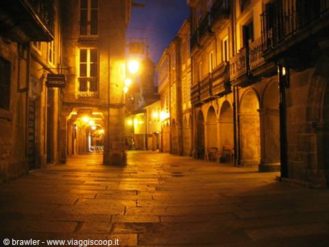 Stone-paved street with arched arcades, lit by street lamps at night
