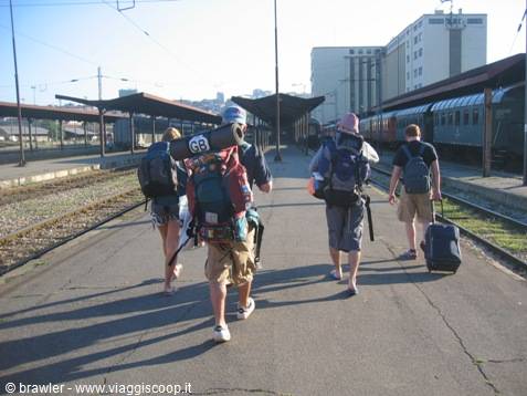 Four backpackers with heavy packs walk along the rails of a railway station