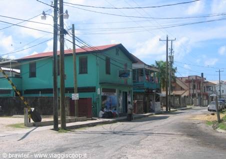 Wooden houses painted green and red along a dusty road with power poles