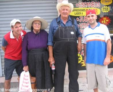 Elderly couple in hat and overalls with two young men outside a shop
