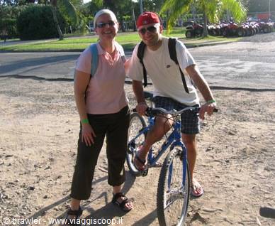 Couple with backpacks beside a blue bicycle on sandy road
