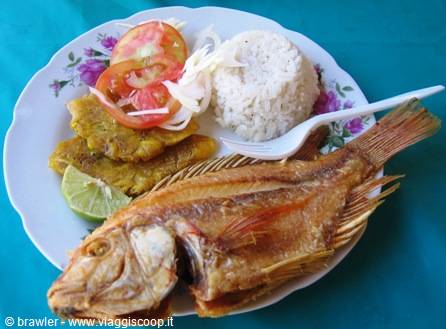 Fried fish plate with rice, patacón, lime slice and salad on blue tablecloth
