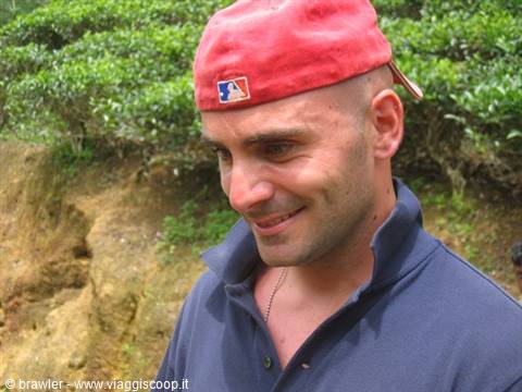 Man in red cap smiling in front of lush tea plantations