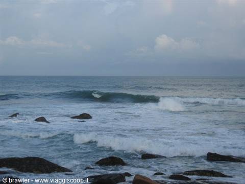 Waves breaking over dark rocks under a cloudy sky