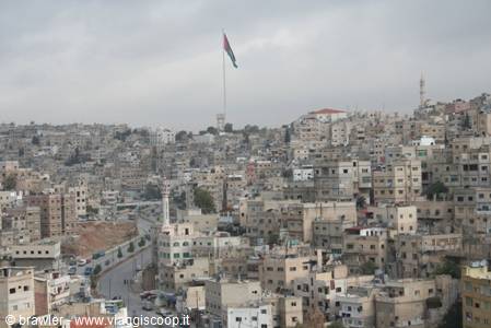 Amman: white concrete buildings under grey sky, Jordanian flag on tall pole