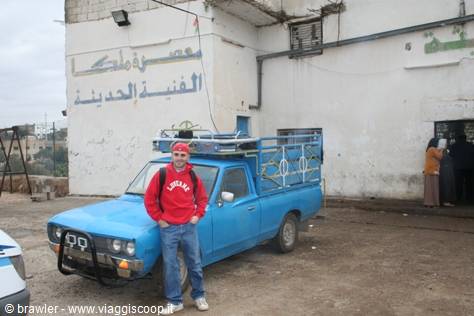 Traveler in red sweatshirt next to a blue pickup in front of a building