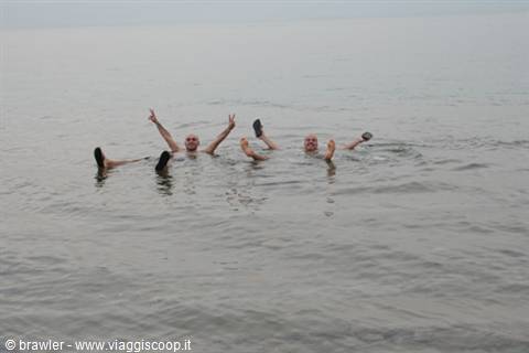Two men float lying on the salty water of the Dead Sea under a grey sky