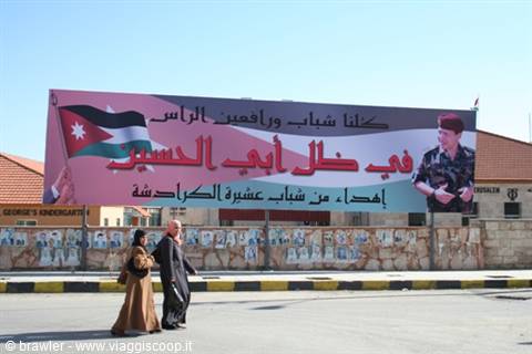 Two women walk past a billboard with the Jordanian flag and King Abdullah's portrait