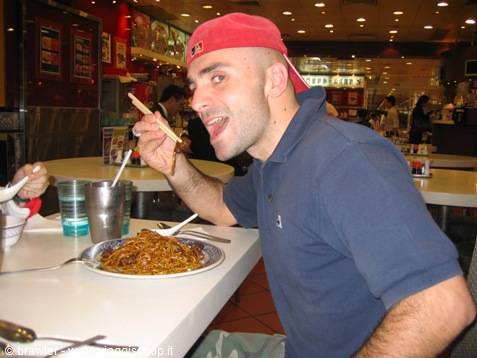 Man in red cap lifts chopsticks in front of a plate of noodles