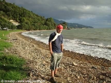 Man in blue shirt and red bandana standing on a pebble beach